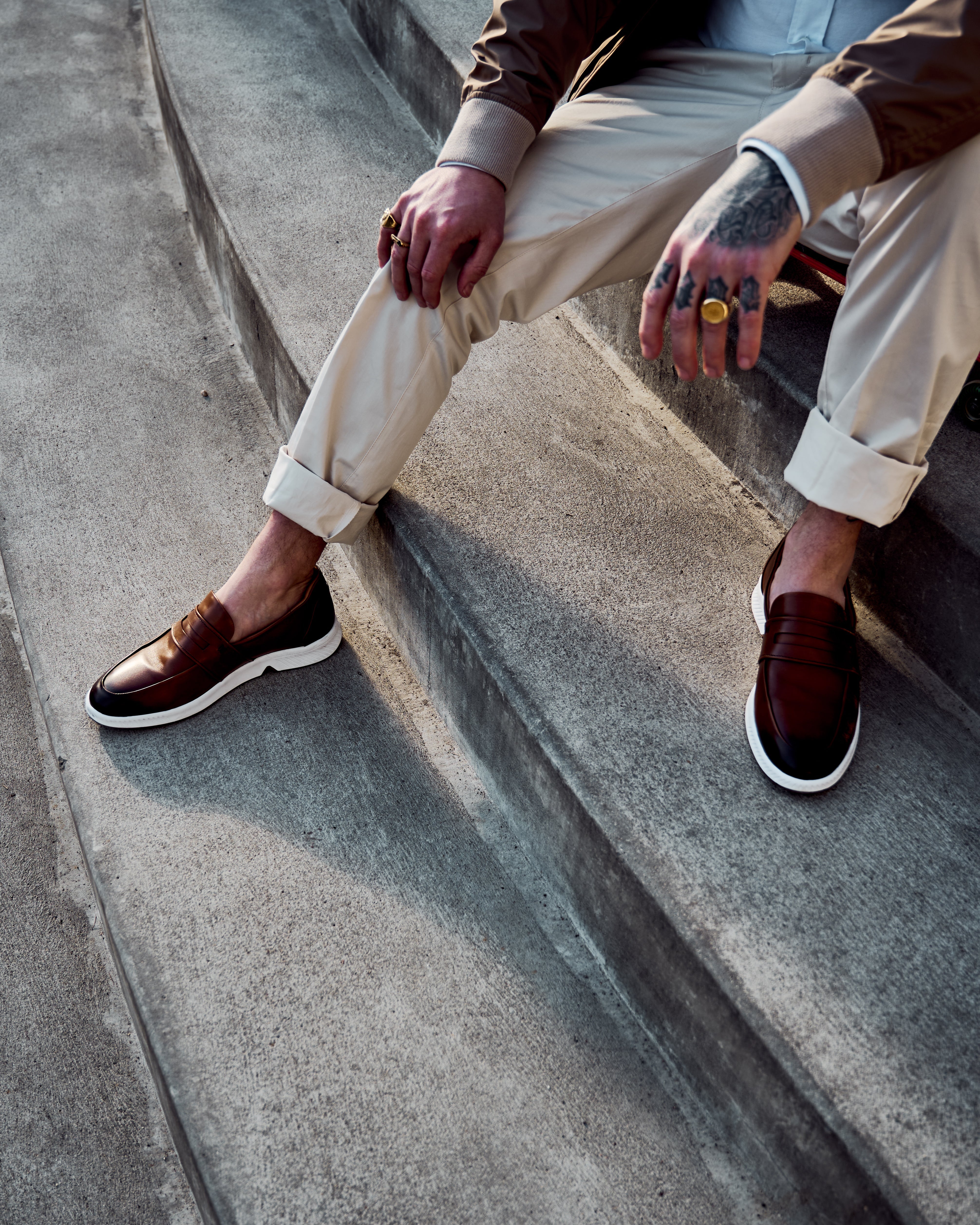 Tattooed skater sitting on steps wearing CHITO in tan. KANREY Loafer shoes in tan.